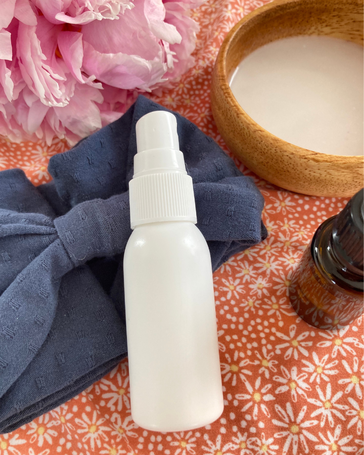 white spray bottle with a hair tie and essential oil and coconut milk
