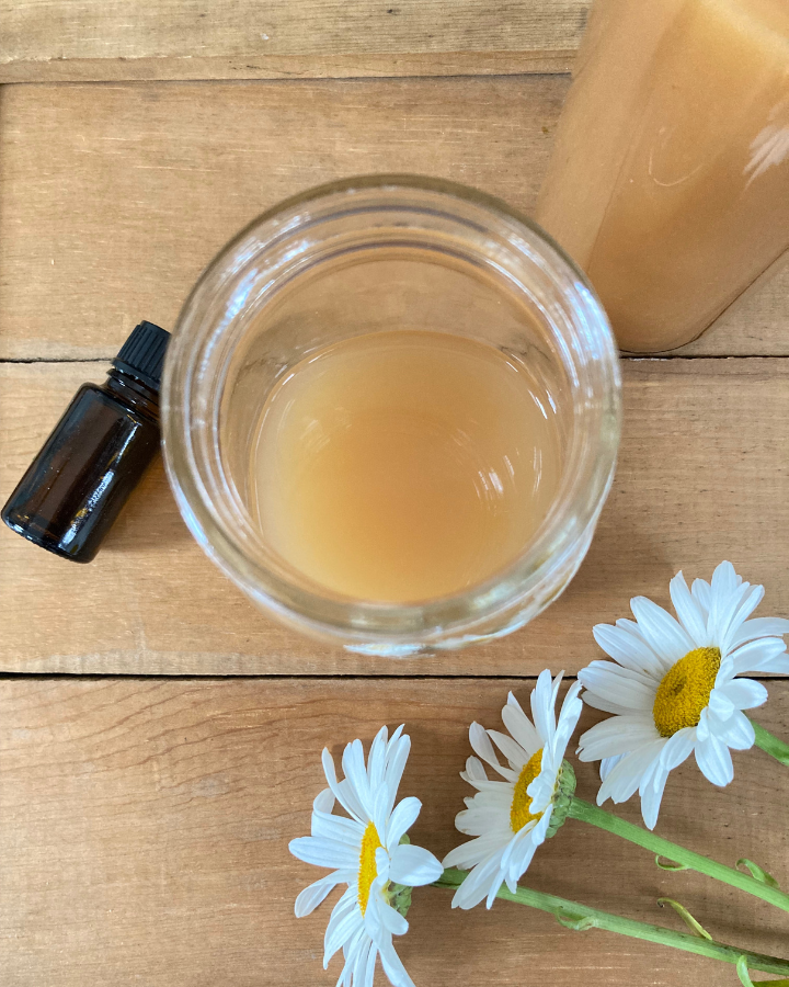 apple cider vinegar hair rinse in a mason jar with flowers and essential oils beside it