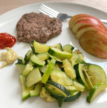 a plate of sauteed zucchini and a hamburger and apple slices
